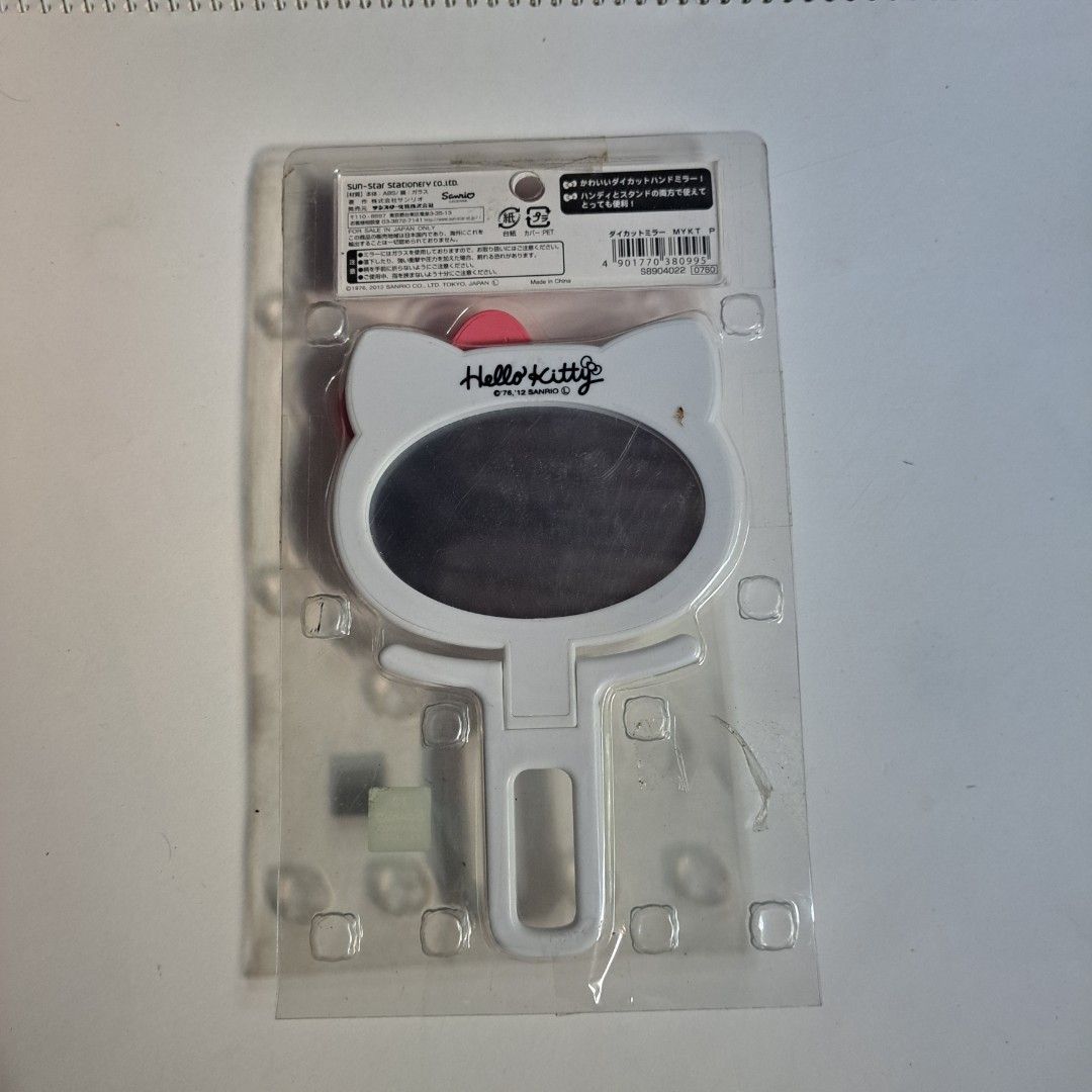 Original Sanrio Hello Kitty Handheld Mirror (Category: Mirrors) located in M'Lang. Submitted by ardinelle.finds (Listing ID 1430858770, Image 2). Description: Kitty handheld mirror. It features a white frame with Kitty's face and a pink bow. The mirror is in its original packaging. The back of the packaging has Japanese text. It has a handle for easy use..