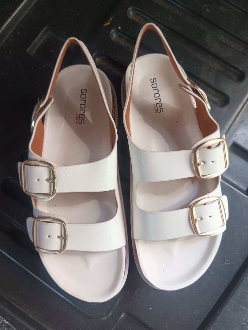 Sorores White Sandals Size 37 (Category: Flats & Sandals) located in Malabon City. Submitted by mslalan (Listing ID 1430806414, Image 1). Description: White Sorores sandals with double buckle straps. The sandals have a cork-like footbed and a thick, white sole. The size is 37, as indicated on the sole. The soles show some signs of wear. The sandals have gold-colored buckles..