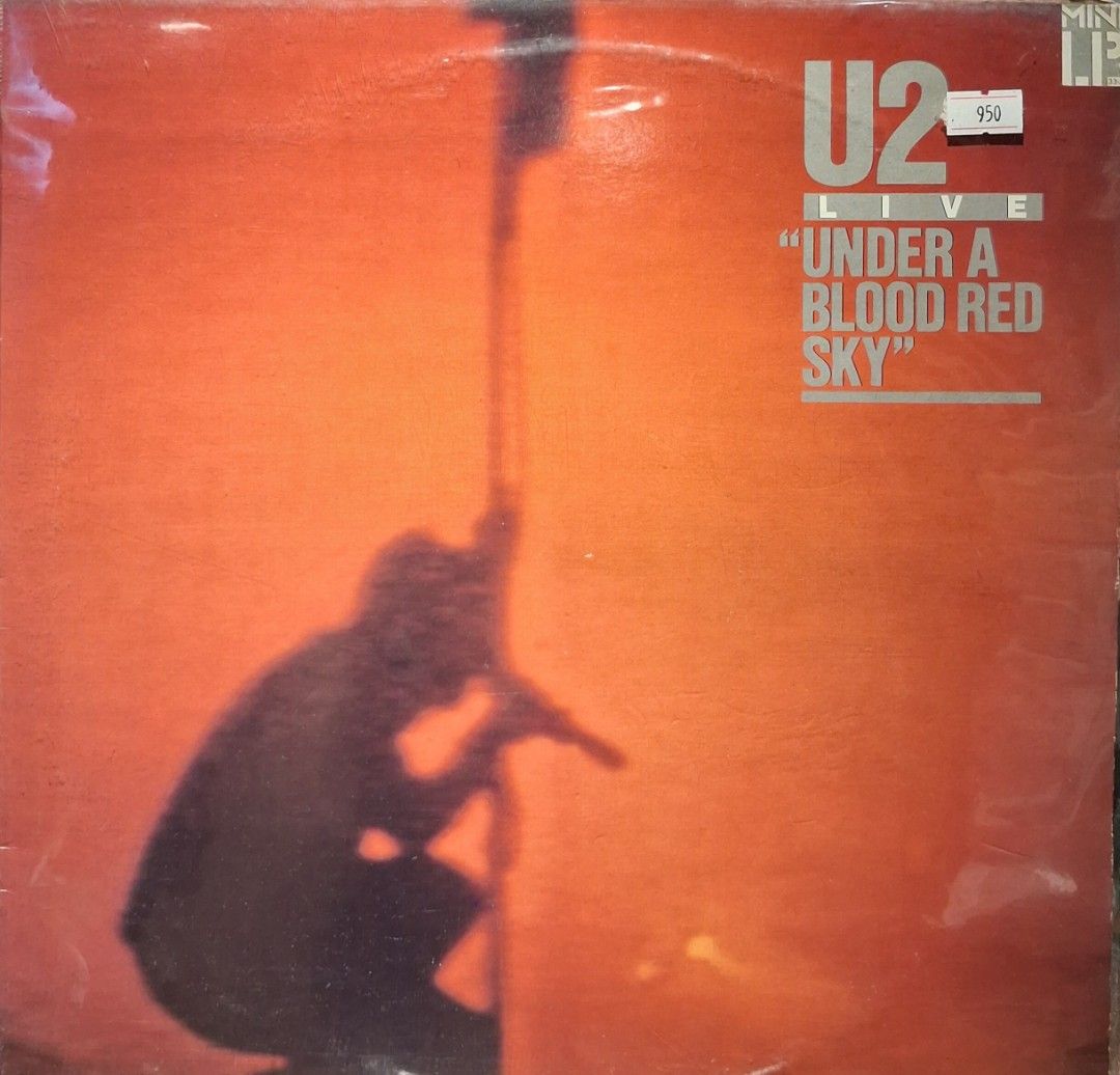 U2 - Under a Blood Red Sky Vinyl Record (Category: Vinyls) located in Quezon City. Submitted by pooh_laa (Listing ID 1430866331, Image 1). Description: U2's live album "Under a Blood Red Sky" on vinyl. Features the iconic album art with a silhouette against an orange background. The album title and band name are clearly visible. A price tag of 950 is present. A great addition for any U2 fan or vinyl collector..