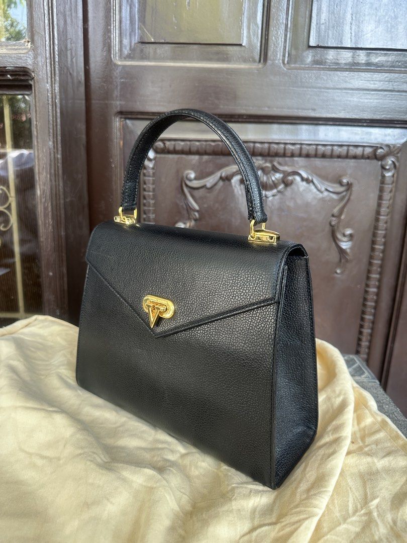 Valentino Garavani Black Handbag (Category: Luxury Bags & Wallets) located in Bustos. Submitted by theprelovedshopbulacan (Listing ID 1430801405, Image 2). Description: Elegant black handbag by Valentino Garavani. Features a top handle and a gold-tone clasp closure. The interior is lined with a fabric that has the Valentino logo. The interior has a small pocket. The brand name is visible on the interior and exterior hardware..