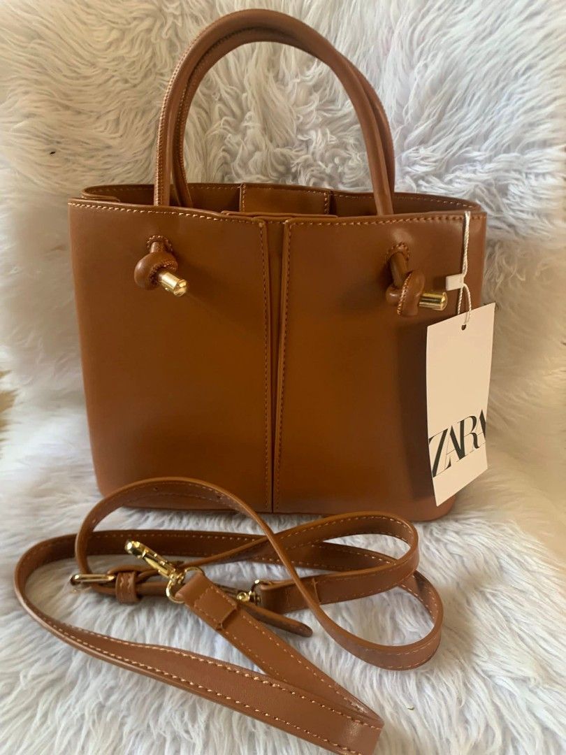 Zara Brown Handbag with Top Handles (Category: Luxury Bags & Wallets) located in Las Pinas. Submitted by ronabelles (Listing ID 1430883752, Image 2). Description: Zara handbag features a structured design with top handles and a detachable shoulder strap. It has a rectangular shape and a rich brown color. The bag includes knot details on the handles and a gold-tone hardware. The bag is suitable for everyday use. Decluttering Brandnew with tag 💙 Z