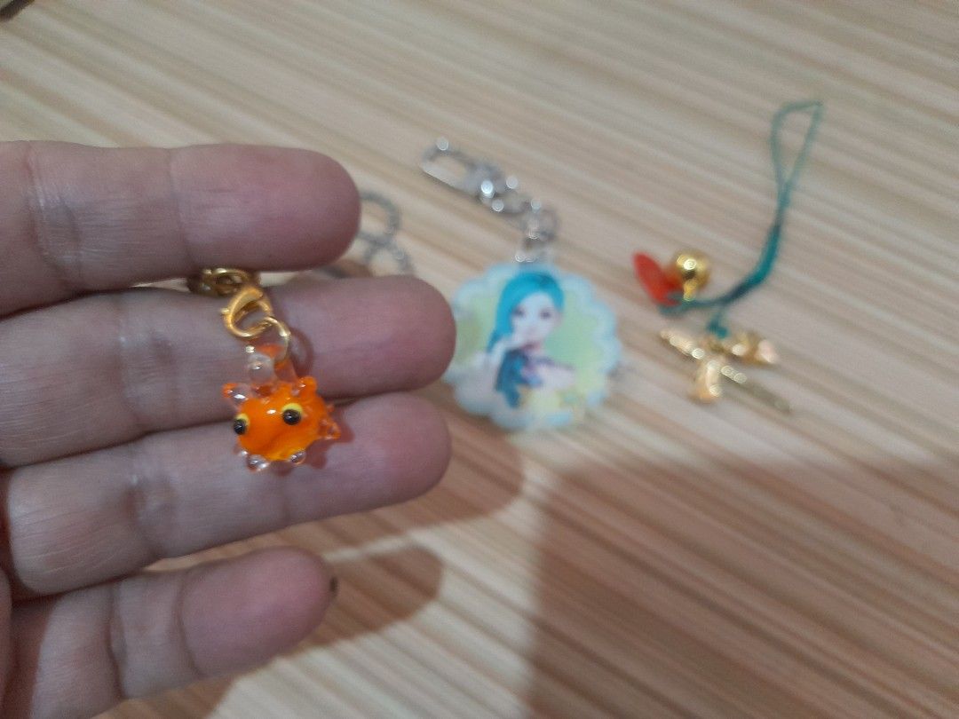 Assorted Keychains (Category: Toys & Games) located in Bocaue. Submitted by marajapansurplus (Listing ID 1431008245, Image 3). Description: Collection of keychains featuring various designs. Includes a black cat, an orange fish, a brown bear-like figure, a girl with blue hair, and a gold-colored cross with a bell. Each keychain has a different attachment style, including a chain, a clasp, and a string. Perfect for adding a touch of personality to