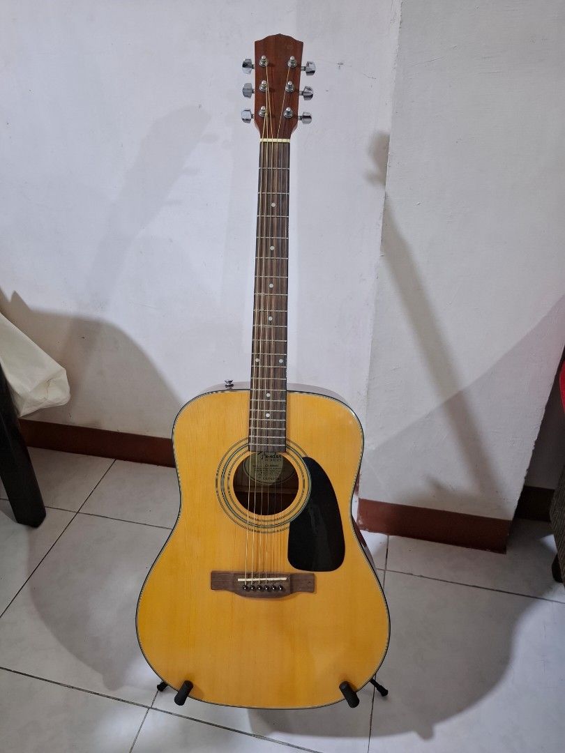 Fender CD-60/NAT Acoustic Guitar (Category: Musical Instruments) located in Mandaluyong City. Submitted by rehenami (Listing ID 1431131723, Image 2). Description: Fender CD-60/NAT acoustic guitar. Includes a guitar stand and a carrying case. The guitar has a natural finish. The headstock has six tuning pegs. The guitar has a black pickguard. The soundhole has a Fender label. The guitar is shown with a capo. With minimal scratches, not noticeable.