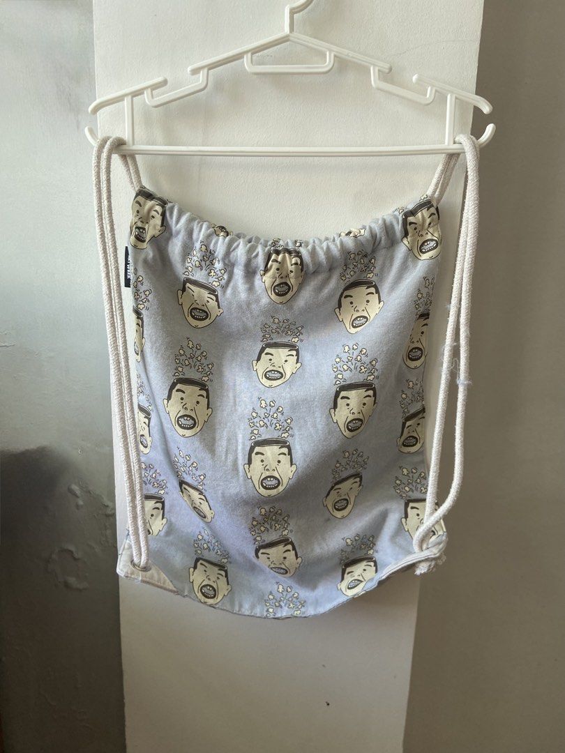 Art Work Drawstring Bag (Category: Backpacks) located in Legazpi City. Submitted by clutterbusterph (Listing ID 1435481827, Image 3). Description: - Unique drawstring bag - Features a repeating face print - White rope straps - Gray fabric - Includes a small black "Art Work" brand tag - Stylish and functional.