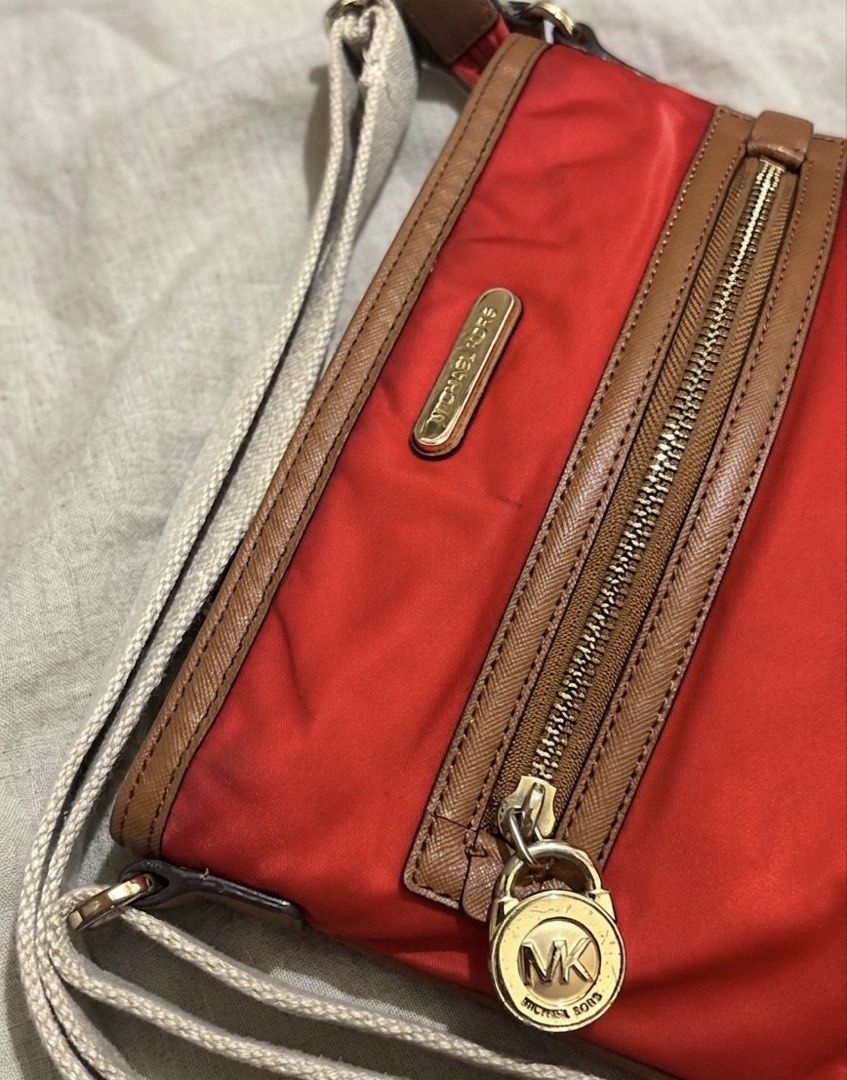 Michael Kors Nylon Crossbody Bag (Category: Cross-body Bags) located in Aparri. Submitted by lpenny (Listing ID 1435509888, Image 2). Description: - Michael Kors crossbody bag - Vibrant red nylon exterior - Brown leather trim - Gold-tone zipper - Signature MK logo - Adjustable strap - Red interior lining - Front zippered pocket - Main compartment (Needs cleaning).