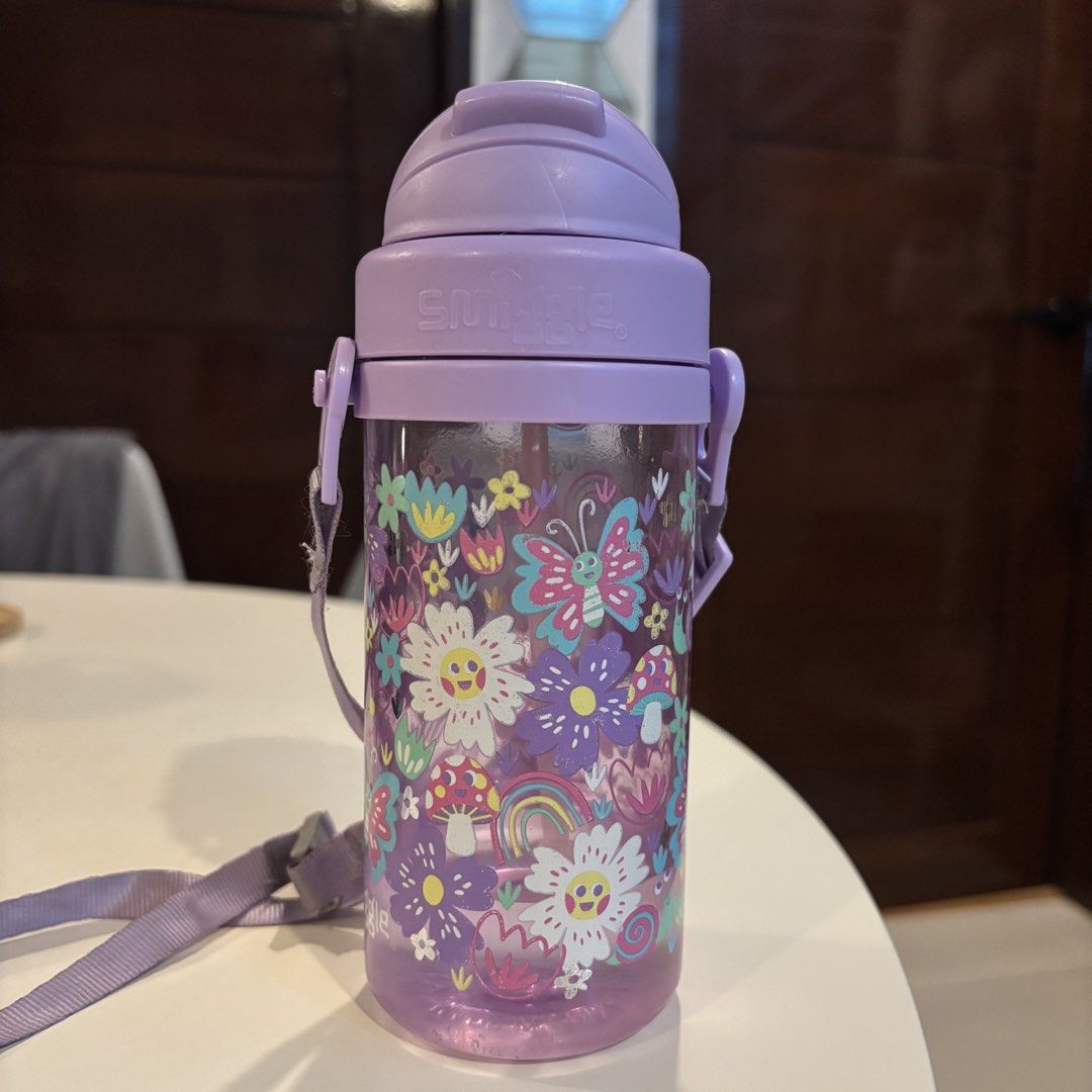 Smiggle Teeny Tiny Plastic Drink Bottle with Strap (Category: Water Bottles & Tumblers) located in Santa Rosa. Submitted by dawnardel16 (Listing ID 1435438162, Image 2). Description: - Smiggle Teeny Tiny Plastic Drink Bottle - Features a colorful floral design - Comes with a purple lid and strap - Secured lid for spill-proof use - Smiggle logo is visible Issues (see photos): - Straw needs to be replaced - cracked lid/cover but can still be used (