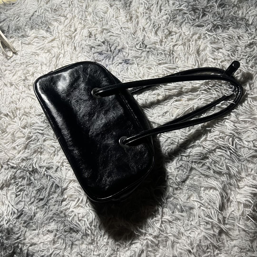 Y2K Glossy Bowler Bag (Black) (Category: Luxury Bags & Wallets) located in Cagayan de Oro. Submitted by ogvarieties (Listing ID 1435462607, Image 1). Description: Model Style: "East-West" Mini Bowler (wider than it is tall). Product Details: - Y2K / Minimalist Vintage. - Jet black faux leather with a high-gloss, "patent" look and a slight wrinkled texture. - Distinctive silver-toned grommets where the straps meet the bag. -Double slim shoulder st