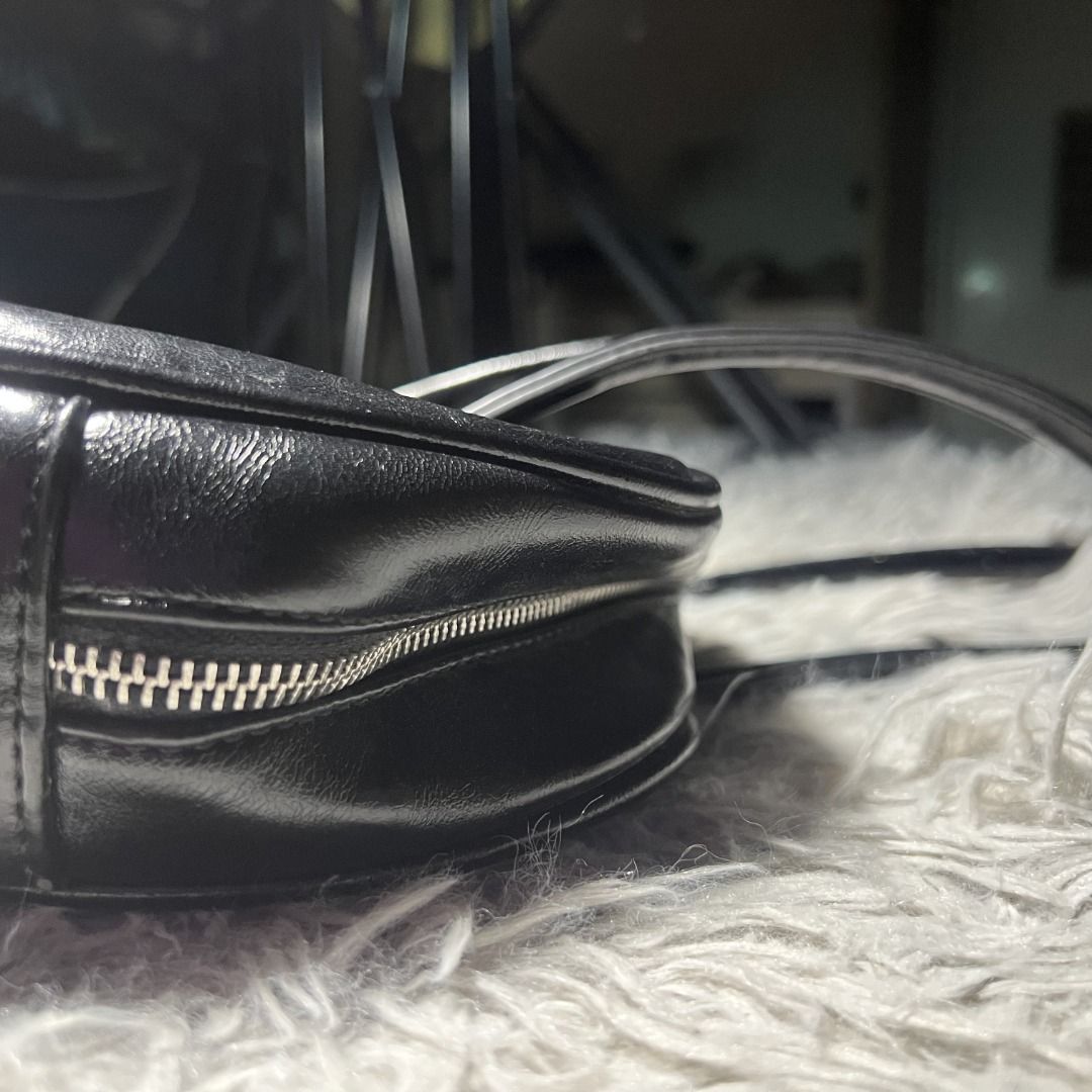 Y2K Glossy Bowler Bag (Black) (Category: Luxury Bags & Wallets) located in Cagayan de Oro. Submitted by ogvarieties (Listing ID 1435462607, Image 3). Description: Model Style: "East-West" Mini Bowler (wider than it is tall). Product Details: - Y2K / Minimalist Vintage. - Jet black faux leather with a high-gloss, "patent" look and a slight wrinkled texture. - Distinctive silver-toned grommets where the straps meet the bag. -Double slim shoulder st