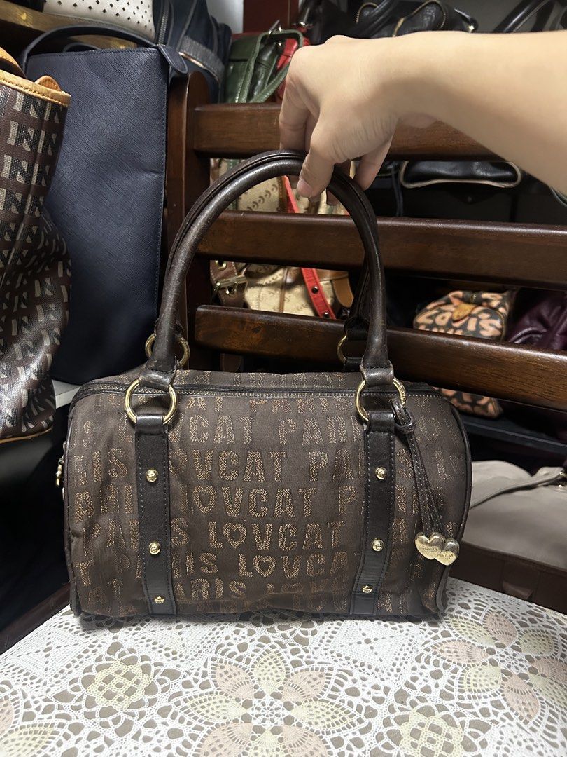 Lovcat Paris Brown Handbag (Category: Luxury Bags & Wallets) located in Lucena. Submitted by blush_lux (Listing ID 1437275091, Image 1). Description: - Authentic Lovcat Paris handbag - Barrel-shaped design - Top handle - Gold hardware accents - Includes a heart charm - Features the repeating Lovcat Paris logo pattern - Dark brown leather trim.