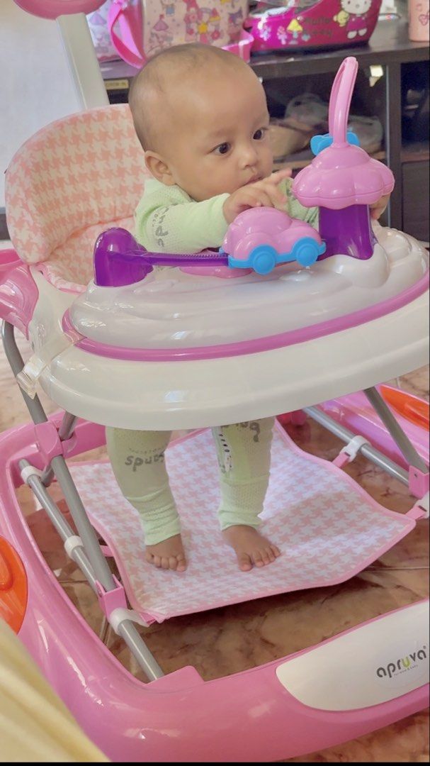 Apruva Baby Walker - Pink (Category: Infant Playtime) located in Caloocan City. Submitted by prettymom05 (Listing ID 1437444972, Image 1). Description: - Pink Apruva baby walker - Features a play area with a car toy - Includes a pink and white patterned seat - Sturdy frame for stability - Comes with a footrest.