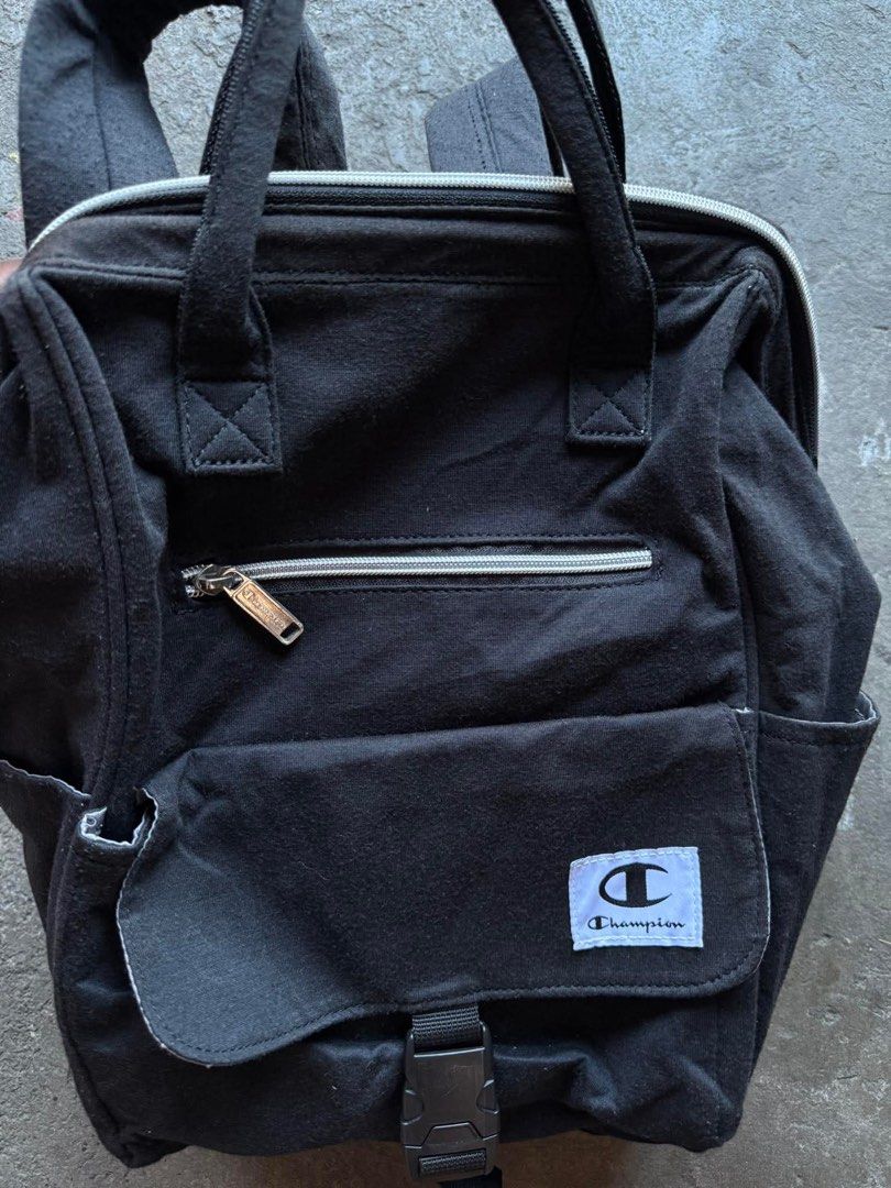 Champion Black Backpack (Category: Backpacks) located in Sariaya. Submitted by IvanYuri07 (Listing ID 1437425224, Image 2). Description: - Black Champion backpack - Top handle and adjustable shoulder straps - Front pocket with buckle closure - Zippered pockets (front and back) - Side pockets - Champion logo on front.