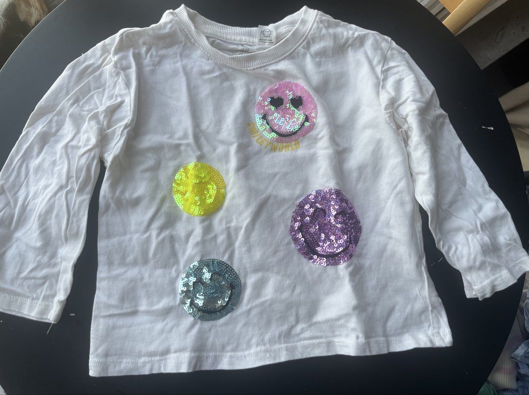 H&M Smiley World Long Sleeve Shirt (Category: Babies & Kids Fashion) located in Mandaluyong City. Submitted by gcr389 (Listing ID 1437459625, Image 1). Description: - White long sleeve shirt - Sequin smiley face design - Features a large "smiley world" graphic - Includes three smaller smiley faces - Crew neck - Long sleeves - Perfect for casual wear - sized 3 to 4yo.