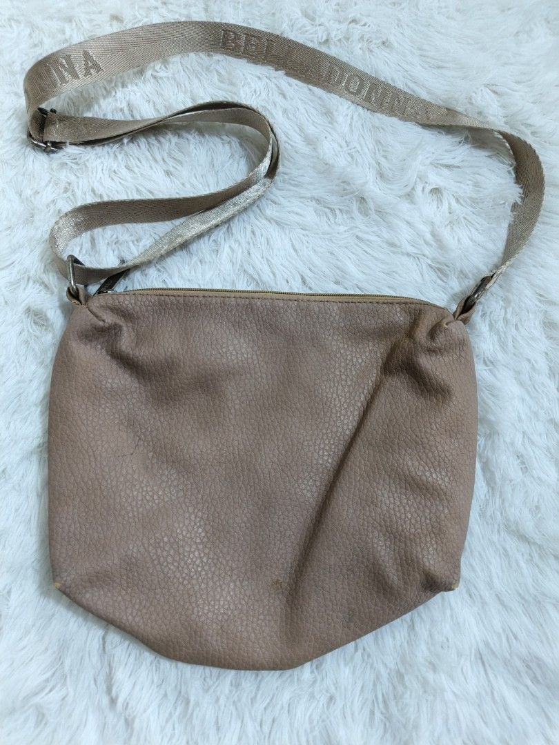 Belladonna Crossbody Bag (Category: Cross-body Bags) located in Marikina City. Submitted by andreah_16 (Listing ID 1437621109, Image 2). Description: - Belladonna crossbody bag - Light brown color - Textured exterior - Long strap with brand name - Zipper closure - Approximately 11 inches wide - Minor wear on bottom corner.