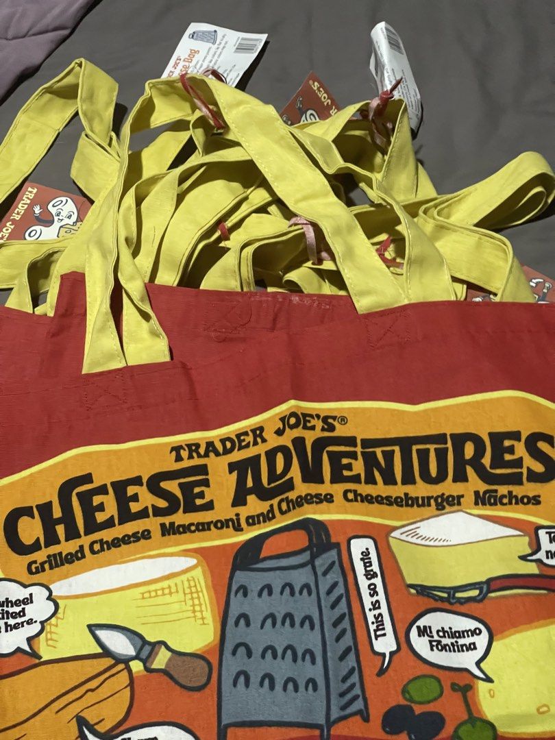 Trader Joe's Cheese Adventures Tote Bag (Category: Tote Bags) located in Paranaque City. Submitted by ces_31 (Listing ID 1437733353, Image 2). Description: - Brand new Trader Joe's Cheese Adventures tote bag. - Features a fun cheese-themed design. - Red background with yellow handles. - Includes graphics of various cheeses and cheese-related items. - Brand new with tags..