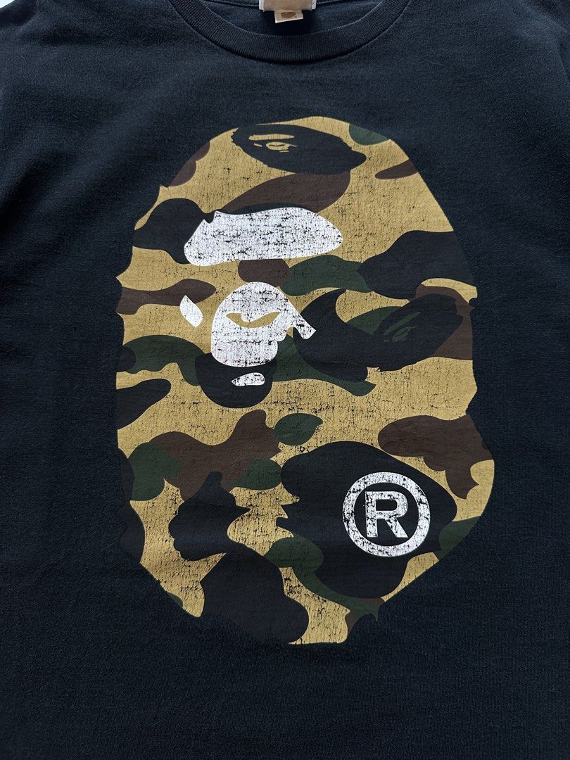 BAPE Camo Ape Head T-shirt (Category: Tshirts & Polo Shirts ) located in Mabalacat. Submitted by shiroe14 (Listing ID 1437840704, Image 2). Description: - Authentic BAPE T-shirt - Features iconic camo ape head design - Black base color - Large camo ape head graphic on front - BAPE logo on sleeve - BAPE logo on neck tag - Size: Large Dimes: 21x27 issue: Crack Print.