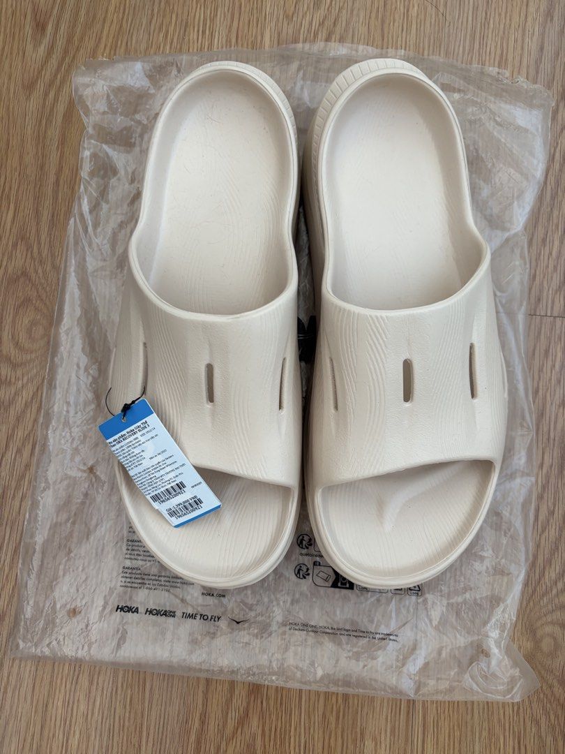 Hoka Recovery Slide 3 - Size 12 (Category: Slippers & Slides) located in Mandaluyong City. Submitted by joebren24 (Listing ID 1437889132, Image 3). Description: - Hoka Recovery Slide 3 sandals - Size: 12 - Color: Light Beige - Condition: New - Comes in original packaging - Features Hoka logo on strap - Packaging includes product information and barcode.