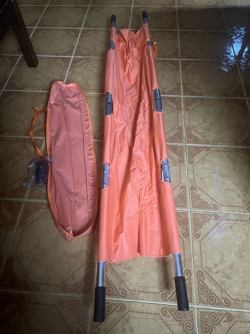 Orange Folding Stretcher with Carrying Bag (Category: Other Assistive Aids) located in Las Pinas. Submitted by jerri44 (Listing ID 1437789536, Image 1). Description: - Orange folding stretcher with matching carrying bag. - Features a sturdy metal frame and handles. - Constructed from durable, water-resistant material. - Folds compactly for storage and portability. - Perfect for emergency situations and medical use..