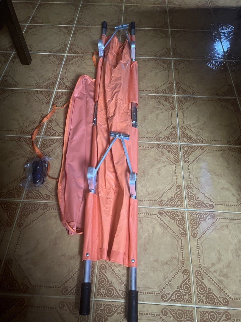 Orange Folding Stretcher with Carrying Bag (Category: Other Assistive Aids) located in Las Pinas. Submitted by jerri44 (Listing ID 1437789536, Image 3). Description: - Orange folding stretcher with matching carrying bag. - Features a sturdy metal frame and handles. - Constructed from durable, water-resistant material. - Folds compactly for storage and portability. - Perfect for emergency situations and medical use..