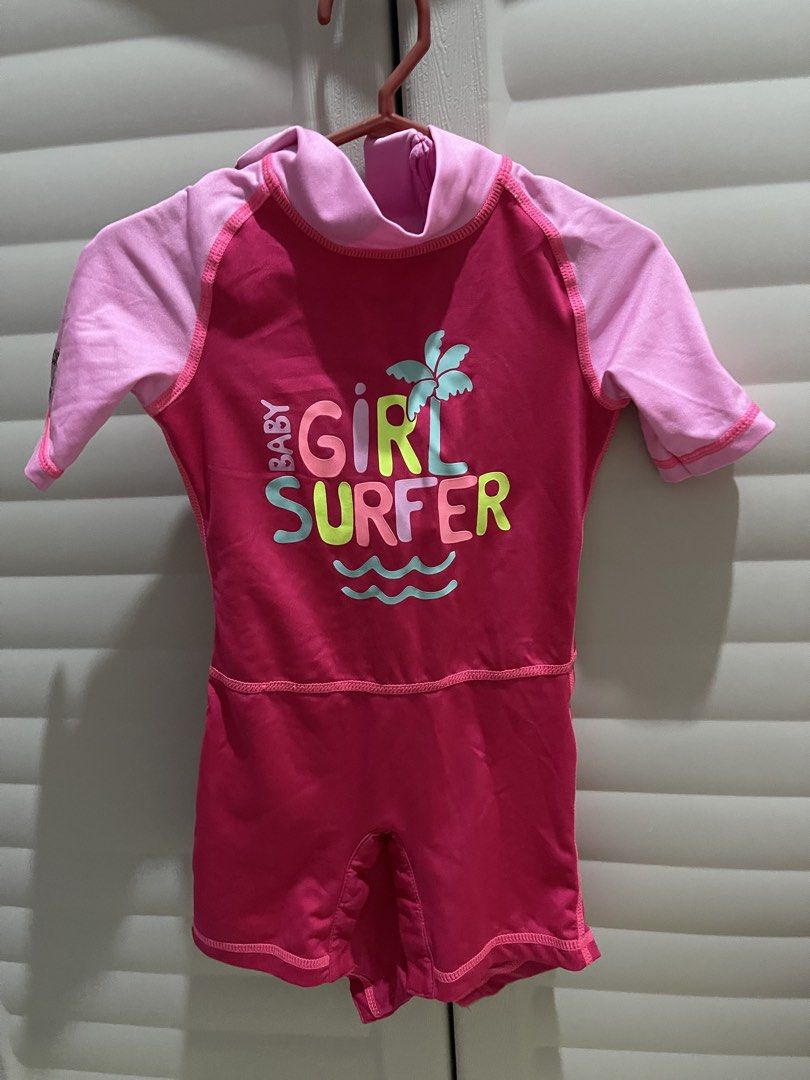 Baby Girl Surfer Swimsuit (Category: Babies & Kids Fashion) located in Imus. Submitted by _o6kath (Listing ID 1438051422, Image 1). Description: - Adorable baby girl swimsuit - Features a vibrant pink and red color scheme - Stylish "Baby Girl Surfer" print on the front - Comfortable short sleeves and high neck design - Made from a stretchy, swim-friendly material - Fun design with palm tree and waves.