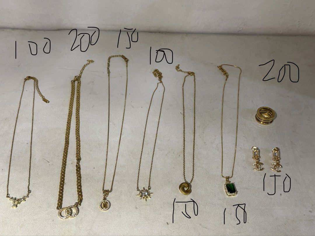 Gold Necklace Collection (Category: Necklaces) located in Marikina City. Submitted by feibella_clothing24 (Listing ID 1438056088, Image 1). Description: Collection of gold necklaces, featuring various designs. Includes a necklace with a pendant, a chain with interlocking circles, a necklace with a sunburst pendant, a necklace with a green stone pendant, and more. Also includes a gold ring and a pair of earrings..