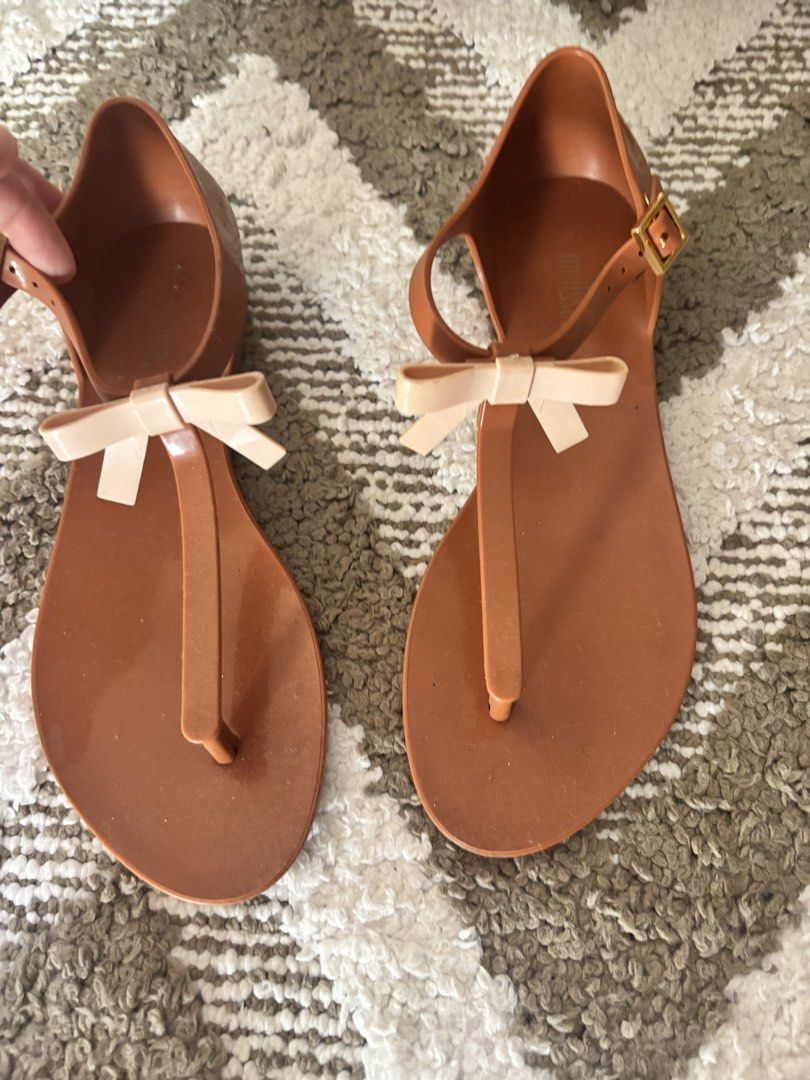 Melissa Sandals with Bow and Bird Design (Category: Flats & Sandals) located in Las Pinas. Submitted by livedog.eb2d1b (Listing ID 1438015409, Image 2). Description: 950 each. Stylish Melissa sandals featuring a bow detail and a bird design. The sandals are brown with a beige bow and a gold buckle. The other pair is a flip-flop style with a bird design. Both pairs are perfect for a casual and chic look..