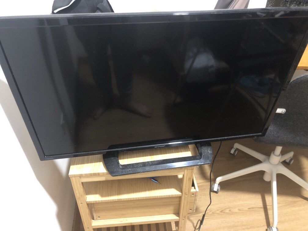 Sharp TV (Category: TV) located in Kuala Lumpur. Submitted by maxluis (Listing ID 1438075783, Image 1). Description: - Sharp TV with black frame - Includes stand - Placed on a wooden shelf - Power cable included.