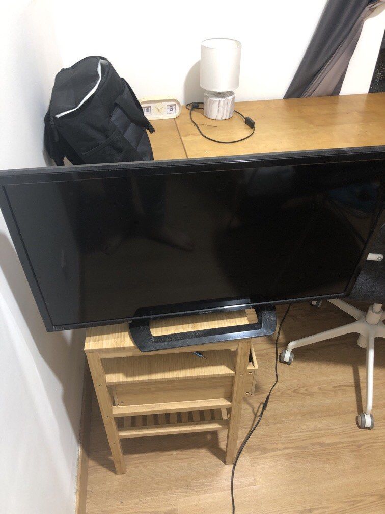 Sharp TV (Category: TV) located in Kuala Lumpur. Submitted by maxluis (Listing ID 1438075783, Image 2). Description: - Sharp TV with black frame - Includes stand - Placed on a wooden shelf - Power cable included.