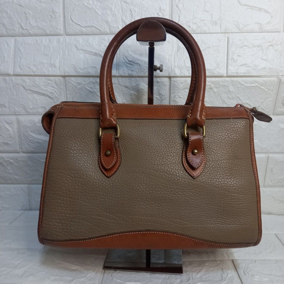Dooney & Bourke Vintage Leather Handbag (Category: Tote Bags) located in Las Pinas. Submitted by etoksi1234 (Listing ID 1438248551, Image 2). Description: Pre-loved Dooney & Bourke Vintage leather handbag in brown and tan. Features a top handle, shoulder strap, zip closure, and logo. Includes metal hardware and feet..
