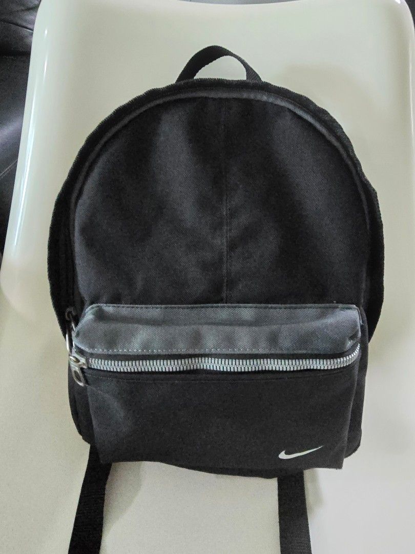 Nike Mini Backpack - Black (Category: Babies & Kids Fashion) located in Singapore. Submitted by november_1231 (Listing ID 1438174708, Image 1). Description: - Black Nike backpack - Small front zip pocket - Adjustable straps - Perfect for carrying essentials - Suitable for primary school books - Features the Nike swoosh.