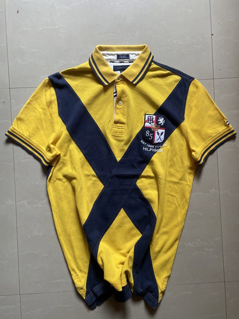 Tommy Hilfiger Polo Shirt (Category: Tshirts & Polo Shirts ) located in Manila. Submitted by cadithrift (Listing ID 1438147541, Image 1). Description: yellow and navy Tommy Hilfiger Custom Fit Polo Shirt with a diagonal cross design and an “85” crest. 20x27 .
