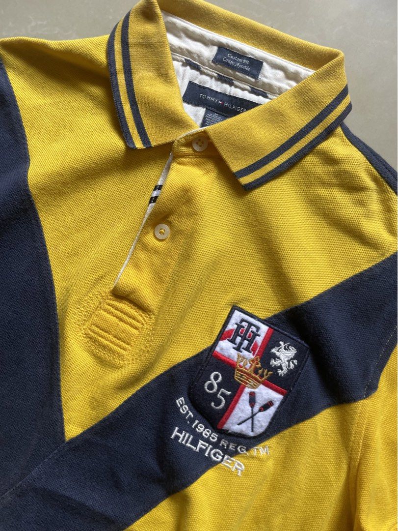 Tommy Hilfiger Polo Shirt (Category: Tshirts & Polo Shirts ) located in Manila. Submitted by cadithrift (Listing ID 1438147541, Image 2). Description: yellow and navy Tommy Hilfiger Custom Fit Polo Shirt with a diagonal cross design and an “85” crest. 20x27 .