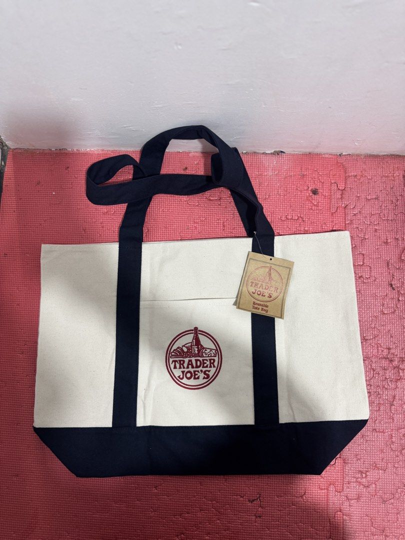 Trader Joe's Canvas Tote Bag (Category: Tote Bags) located in Valenzuela. Submitted by fairythrift (Listing ID 1438138131, Image 2). Description: Trader Joe's tote bag Large Ideal for groceries or beach trips Features a navy blue base and handles Includes a front pocket Features the Trader Joe's logo.