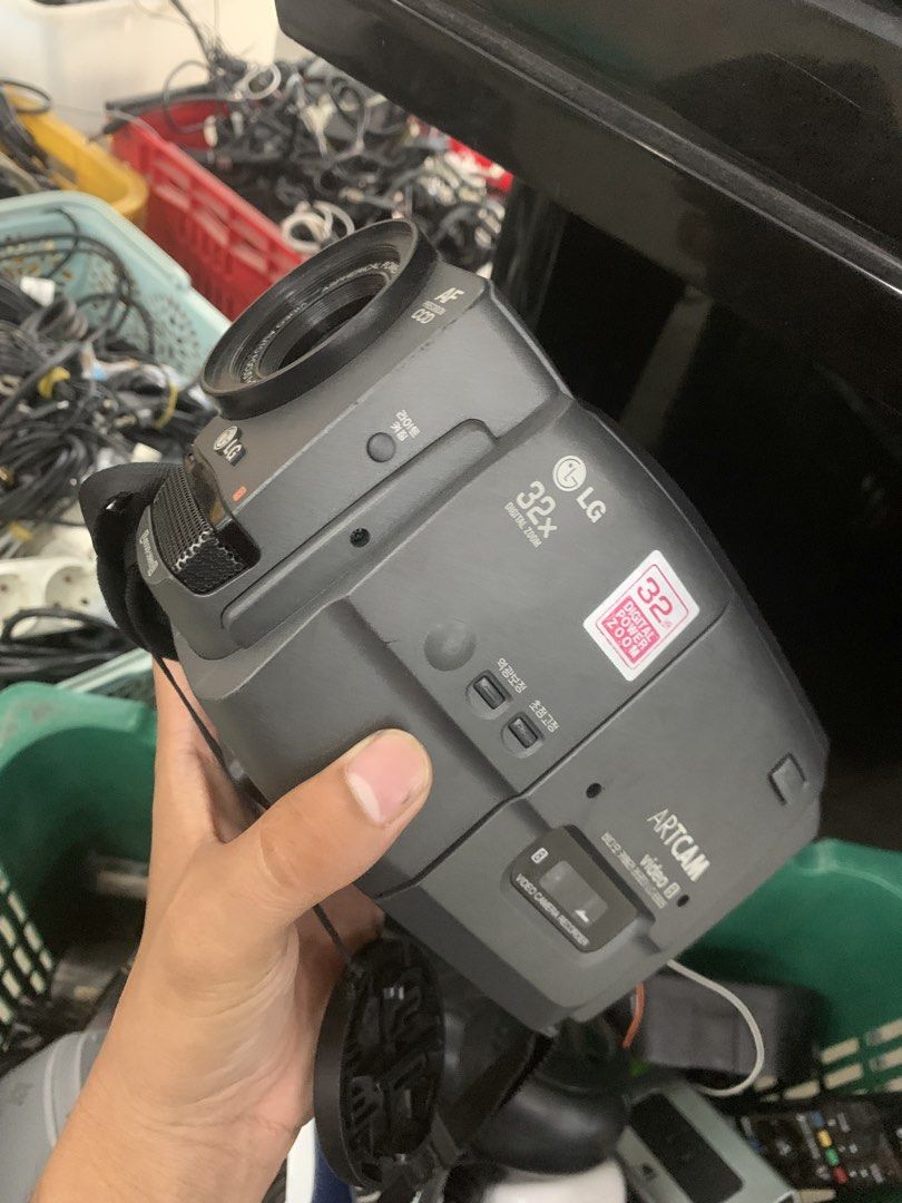 LG Artcam Video 8 Camcorder (Category: Video Cameras) located in Manila. Submitted by 0thrift_n_isaw (Listing ID 1438411886, Image 1). Description: LG Artcam Video 8 camcorder with 32x digital zoom. Features a built-in viewfinder and a hand strap for easy carrying. Includes a '32' sticker. The camcorder has various buttons and ports. The model number is LC-E835. It has a grey and black color scheme..