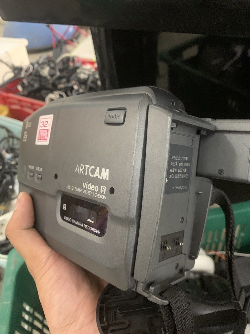 LG Artcam Video 8 Camcorder (Category: Video Cameras) located in Manila. Submitted by 0thrift_n_isaw (Listing ID 1438411886, Image 2). Description: LG Artcam Video 8 camcorder with 32x digital zoom. Features a built-in viewfinder and a hand strap for easy carrying. Includes a '32' sticker. The camcorder has various buttons and ports. The model number is LC-E835. It has a grey and black color scheme..