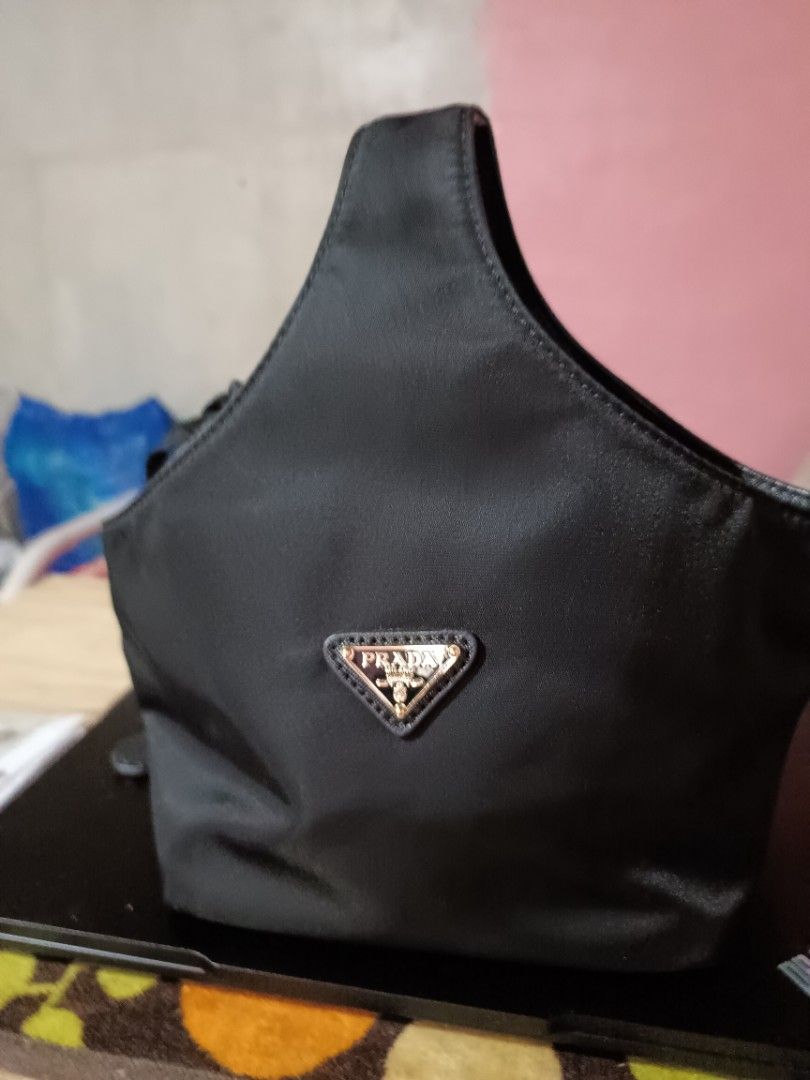 Prada Black Handbag (Category: Luxury Bags & Wallets) located in Taguig. Submitted by blessedlupie (Listing ID 1438333141, Image 1). Description: - Authentic Prada handbag - Color: Black - Features the iconic triangular Prada logo in gold - Single handle design - Unique rounded shape - Crafted from a smooth, possibly nylon, material.
