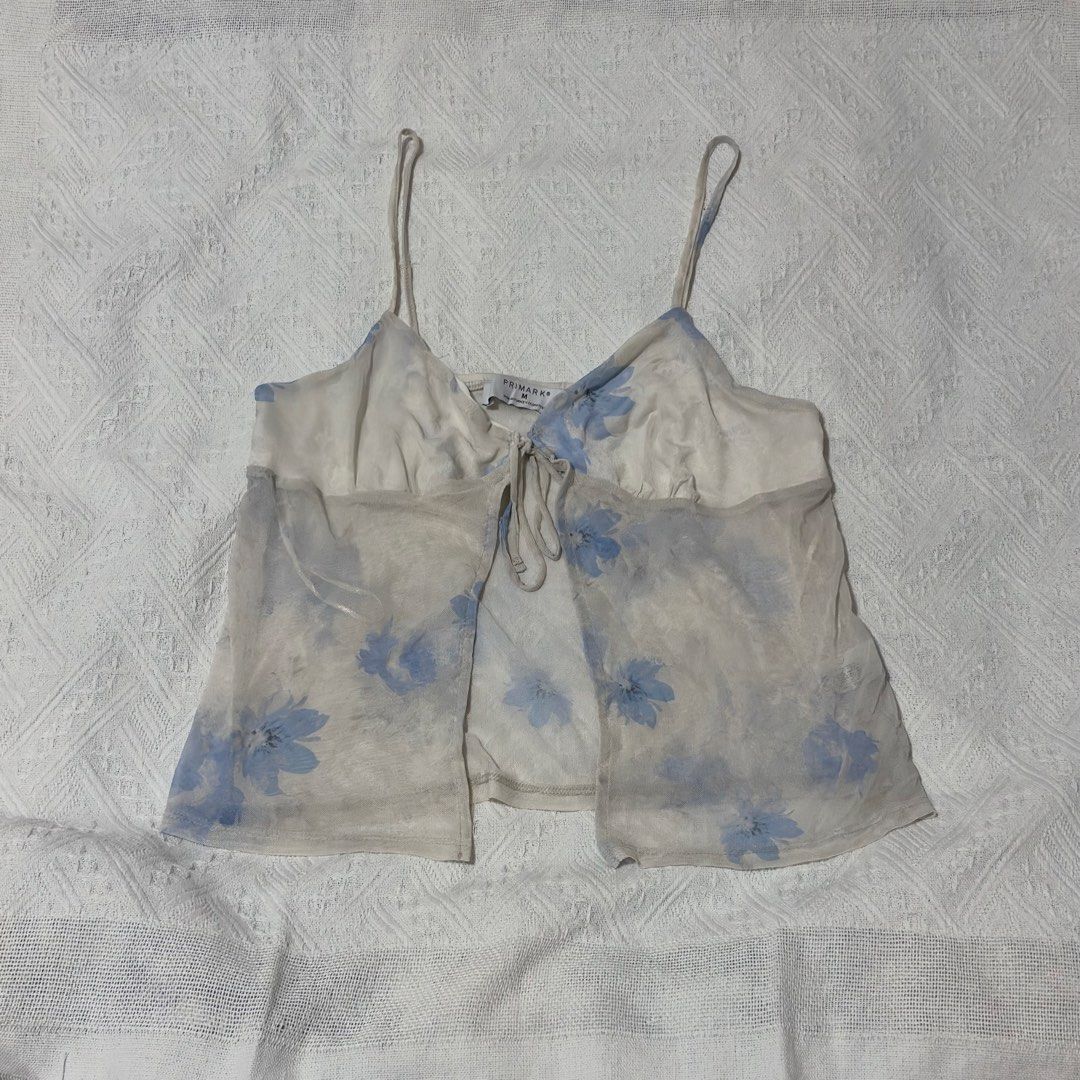 Primark Beach Summer Floral Tie-Front Top (Category: Blouses) located in Pateros City. Submitted by evenings_ (Listing ID 1438485970, Image 2). Description: - Double fabric on the bust part so it’s not see through - Primark floral top, size M. - Delicate floral print with a tie-front design. - Features spaghetti straps and a sheer overlay. - Lightweight fabric, ideal for warm weather. - White base with blue floral details. - Made in Turkey..