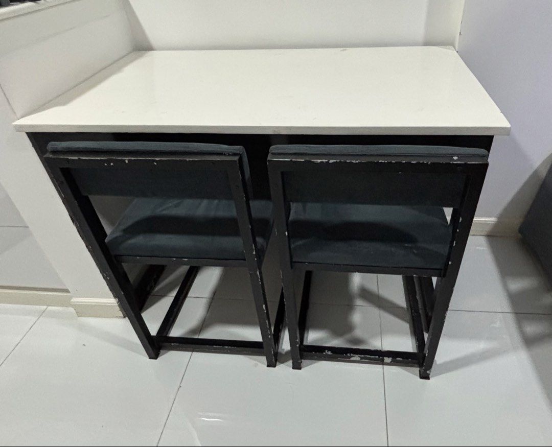 Small Dining Table for 4-5 (Category: Tables & Sets) located in Makati City. Submitted by katrina_00 (Listing ID 1438410537, Image 3). Description: - Compact dining table set - Whites tabletop with black metal frame - Includes two chairs + 1 bench - Chairs have dark grey-green cushioned seats - Table and chairs nest for space-saving storage - Great for small apartments and studios Depth: 61cm Length: 111.5cm Height: 75cm Needs a primer and paint 