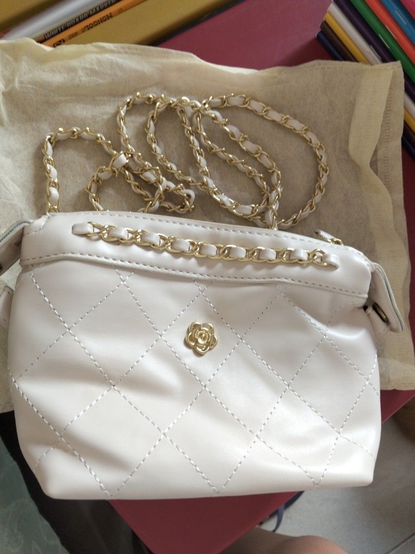 White Quilted Handbag with Gold Chain (Category: Cross-body Bags) located in Marikina City. Submitted by mbf0911 (Listing ID 1438379829, Image 1). Description: - White handbag/crossbody bag - Gold chain strap and top handle - Decorative flower emblem - Smooth, leather-like material - Zipper closure - Gold chain detail.