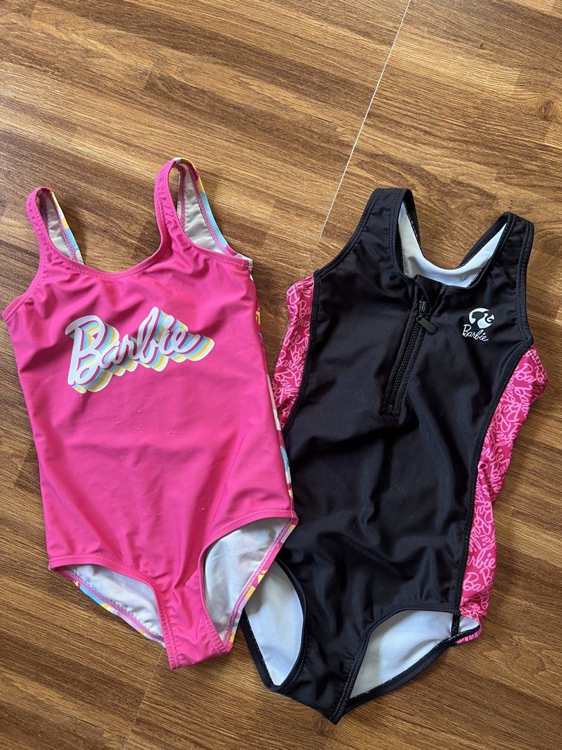 Barbie Swimsuit Set (Category: Bikinis & Swimsuits) located in Caloocan City. Submitted by pmaerc (Listing ID 1438594205, Image 1). Description: - Two Barbie swimsuits for kids. - One is pink with the Barbie logo; shows some wear on the front. - The other is black with pink accents and a zipper. - Both swimsuits have a Barbie logo. -Pink size small: Black size medium.