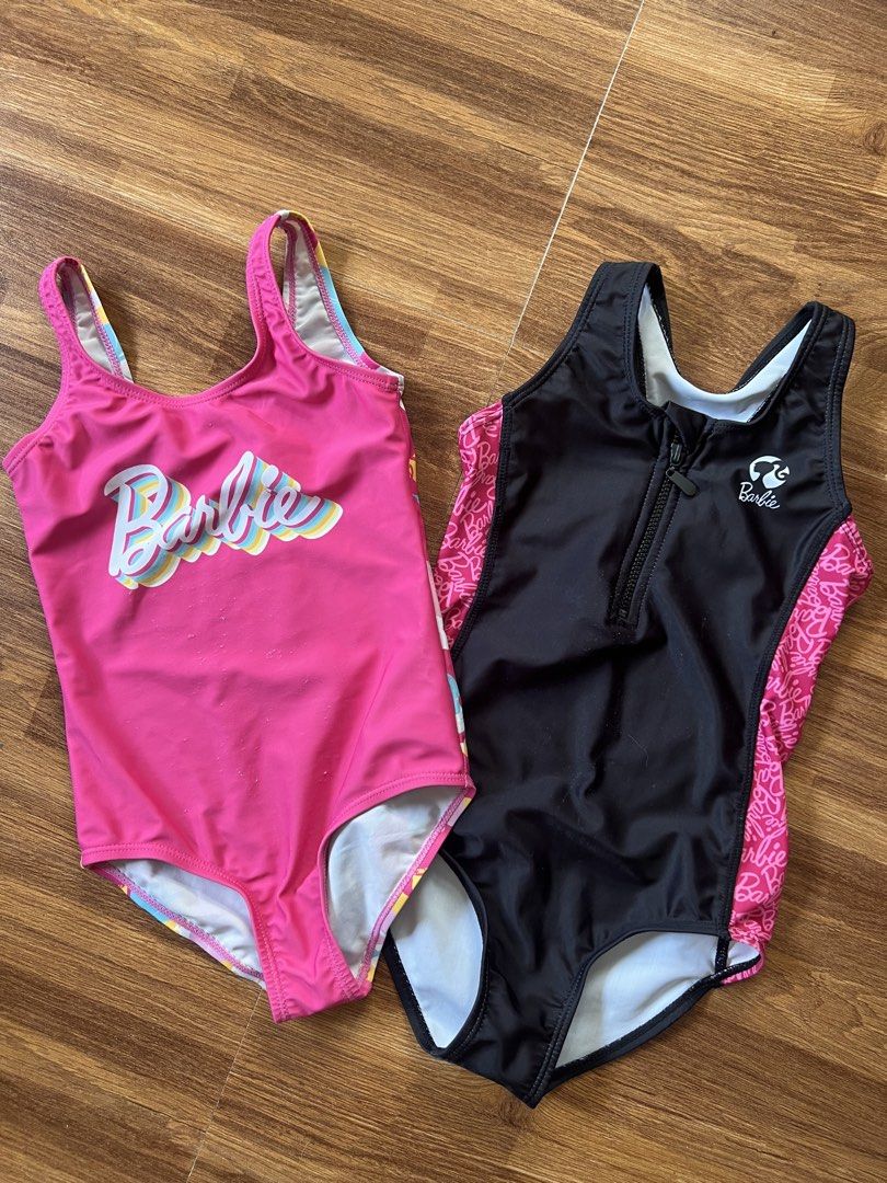 Barbie Swimsuit Set (Category: Bikinis & Swimsuits) located in Caloocan City. Submitted by pmaerc (Listing ID 1438594205, Image 2). Description: - Two Barbie swimsuits for kids. - One is pink with the Barbie logo; shows some wear on the front. - The other is black with pink accents and a zipper. - Both swimsuits have a Barbie logo. -Pink size small: Black size medium.