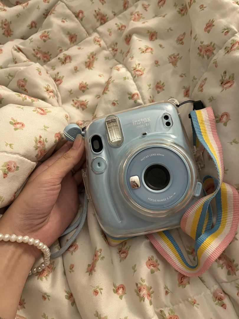 Fujifilm Instax Mini 11 - Sky Blue (Category: Cameras) located in Tagum. Submitted by butterfinger21 (Listing ID 1438687445, Image 1). Description: - Fujifilm Instax Mini 11 in Sky Blue - Includes matching strap with colorful design - Comes with a clear protective case - Focus range: 0.3m to infinity - Instax logo visible.