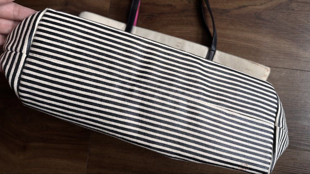 Kate Spade New York Tote Bag (Category: Tote Bags) located in Mandaluyong City. Submitted by TheWeekendProject (Listing ID 1438566438, Image 3). Description: - Kate Spade tote bag - Black and white striped bottom - Black handles with pink accents - Cream-colored body - Pink Kate Spade logo - Visible stains on exterior - Suitable for everyday use.