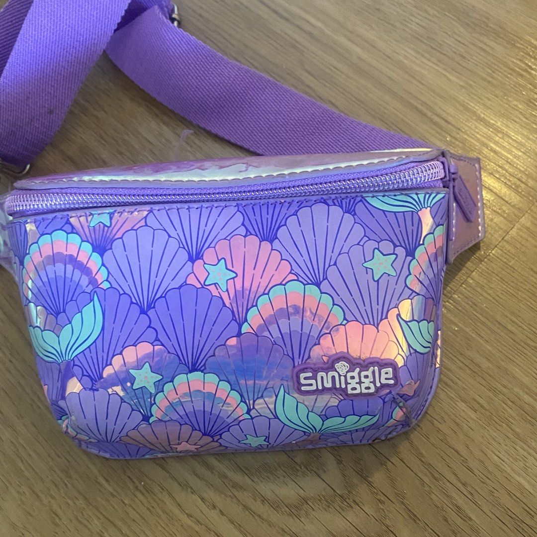 Smiggle Mermaid Waist Bag (Category: Babies & Kids Fashion) located in Paranaque City. Submitted by kalattt (Listing ID 1438559679, Image 1). Description: - Smiggle mermaid waist bag - Purple and iridescent design - Zippered main compartment - Adjustable strap - Adorned with seashell and star patterns - Smiggle logo visible.