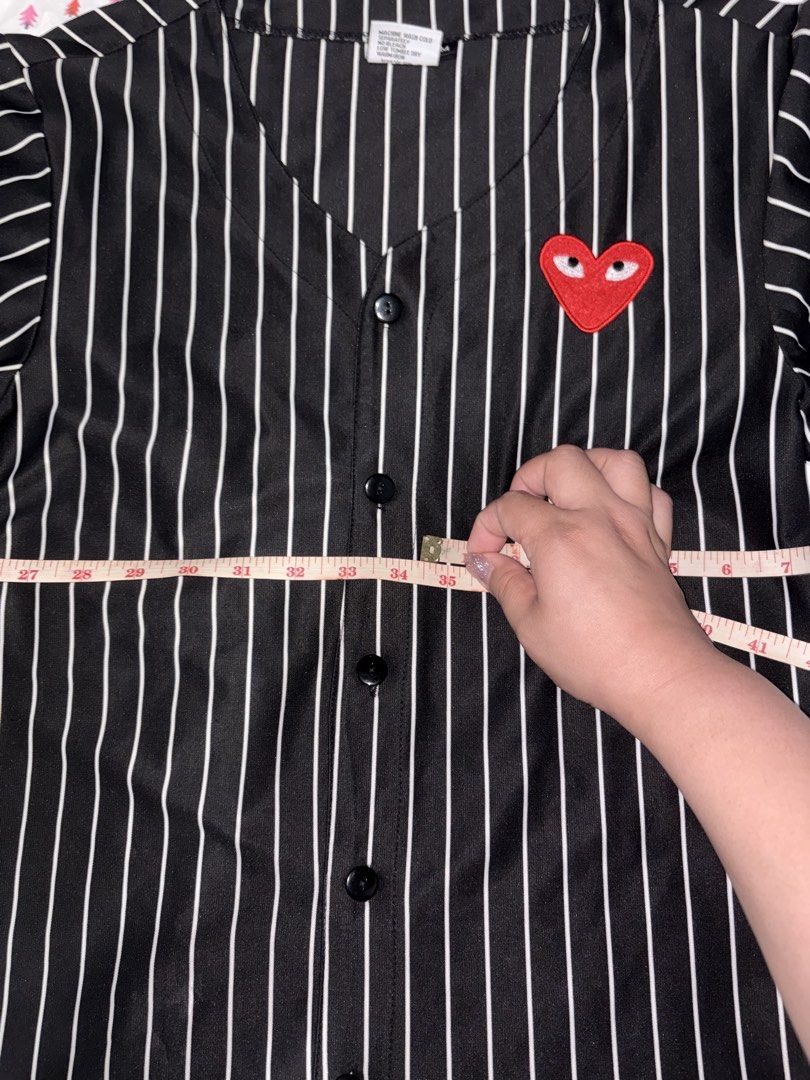 Comme des Garçons Striped short sleeve button down shirt (Category: Shirts) located in Manila. Submitted by fierce_denclutter (Listing ID 1438641783, Image 3). Description: - Black and white striped baseball shirt - Features a red heart patch - V-neck design - Button-up closure - Short sleeves - Length: Approximately 27 inches - Chest width: Approximately 35 inches.