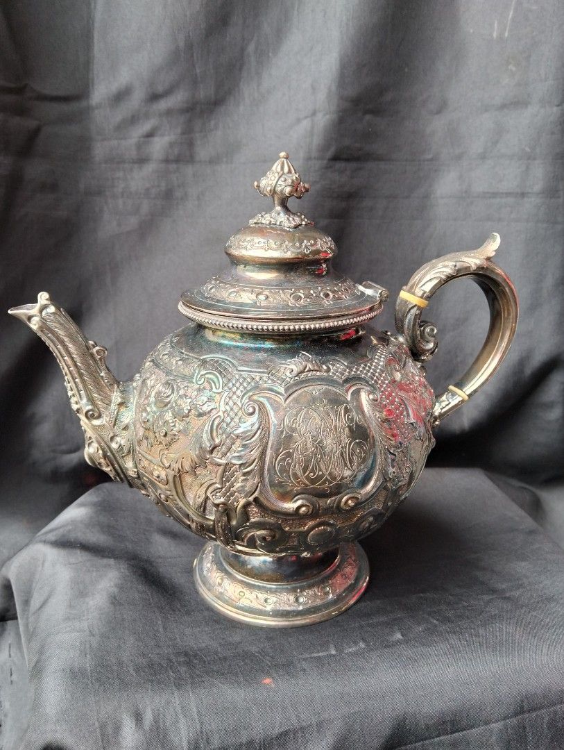 Antique Silver Teapot with Detailed Engravings (Category: Coffee & Tea Tableware) located in Manila. Submitted by raymundm36884 (Listing ID 1438730133, Image 2). Description: - Antique silver teapot - Intricate floral and figural engravings - Decorative lid and handle - Approximately 10 inches tall - Weighs around 995 grams - Perfect for display or use.