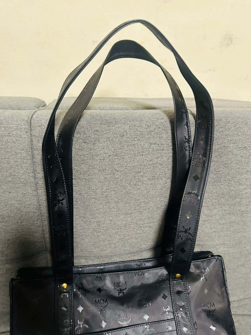 MCM Black Tote Bag (Category: Luxury Bags & Wallets) located in Bulacan. Submitted by alfredcarp0905 (Listing ID 1438707333, Image 2). Description: - Authentic MCM tote bag - Features the brand's signature logo pattern - Equipped with two shoulder straps - Secure top zipper closure - Elegant gold-colored hardware - Constructed from a durable, possibly coated, material.