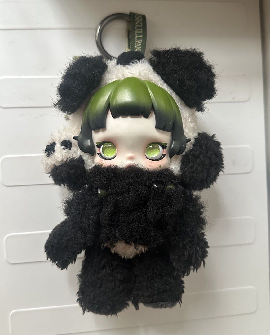 Popmart SkullPanda Lazy Panda Doll Keychain (Category: Plushies & Soft Toys) located in Quezon City. Submitted by shopalmostfriday (Listing ID 1438694059, Image 1). Description: - Adorable Skull Panda doll keychain. - Features a panda plushie with a doll face. - Doll has green hair and green eyes. - Panda plushie has black and white fur. - Includes a keychain ring for easy attachment. - Comes with a small bamboo charm. - with blister box.