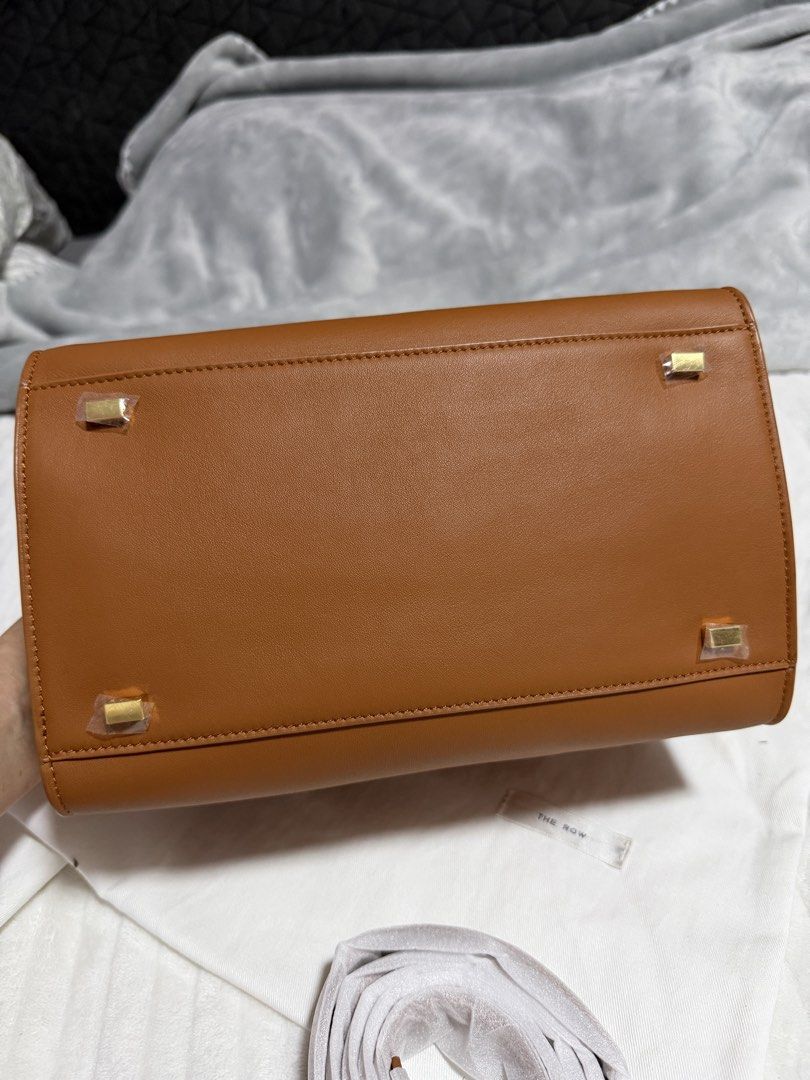 The Row Half Moon Bag (Category: Luxury Bags & Wallets) located in Angono. Submitted by annabela8910 (Listing ID 1438853040, Image 2). Description: - The Row Half Moon bag in a warm tan color. - Structured design with top handle and detachable shoulder strap. - Light-colored fabric interior. - Protective wrapping on handles and feet. - Minimalist design with gold-toned hardware. .