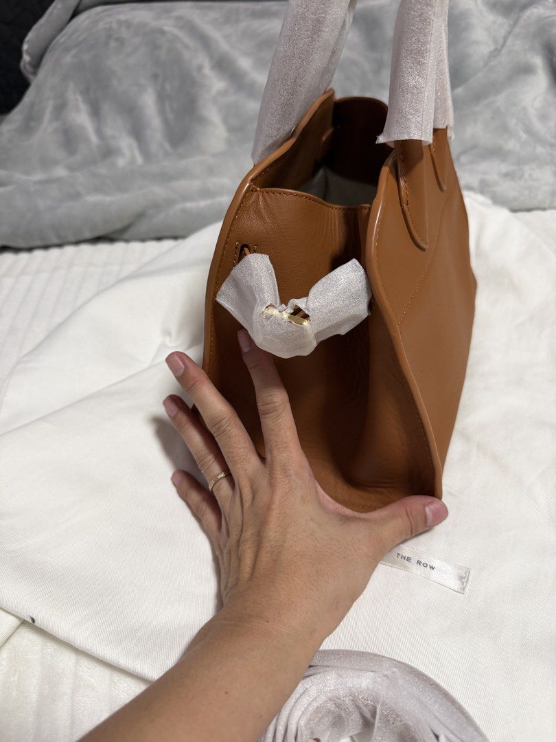 The Row Half Moon Bag (Category: Luxury Bags & Wallets) located in Angono. Submitted by annabela8910 (Listing ID 1438853040, Image 3). Description: - The Row Half Moon bag in a warm tan color. - Structured design with top handle and detachable shoulder strap. - Light-colored fabric interior. - Protective wrapping on handles and feet. - Minimalist design with gold-toned hardware. .