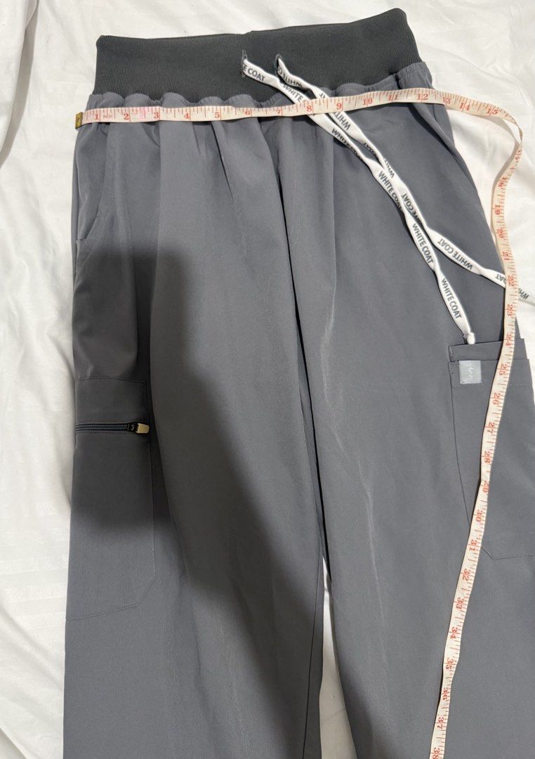 White Coat Gray Scrub Pants (Category: Other Bottoms) located in Manila. Submitted by drewgreig95 (Listing ID 1438854085, Image 2). Description: - White Coat gray scrub pants - Waist: Approximately 30 inches - Length: Approximately 39 inches - Drawstring waistband - Multiple pockets (including a zippered pocket) - Smooth, likely synthetic material - Relaxed fit.